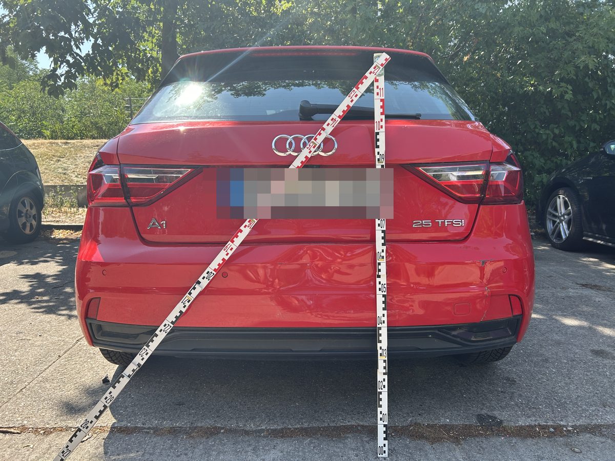 Heckansicht eines roten Audi A1 mit eingedrücktem Heck und angelegten Messlatten, Kennzeichen unkenntlich gemacht, Schadenhöhe 11.668,25 €